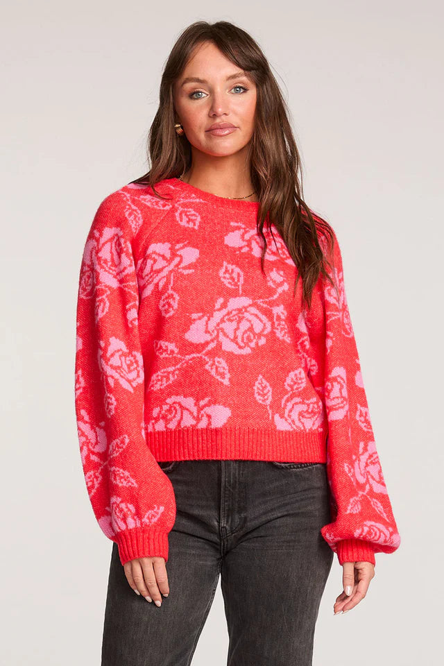 Woman wearing a red sweater with white floral patterns on a plain background