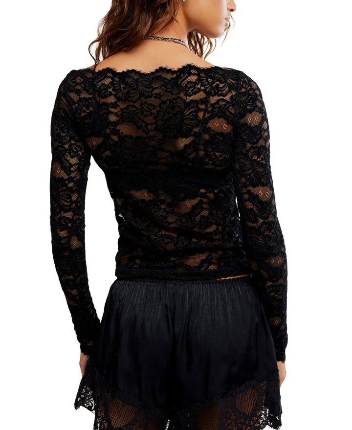 A woman shown from the back wearing a black lace long-sleeve top and a black skirt against a plain white background.