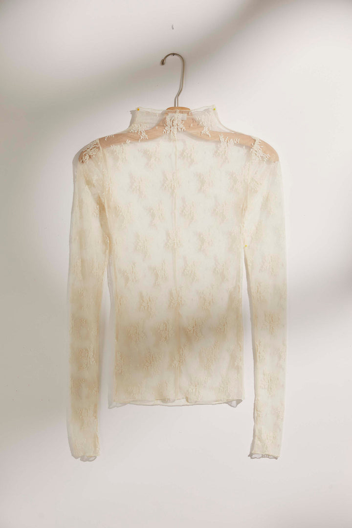 A cream-colored sheer lace long-sleeve top with a mock neck, hanging on a wooden hanger against a plain light background.