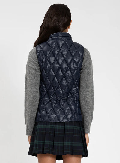 Person wearing a navy quilted vest over a gray sweater and plaid skirt on a white background
