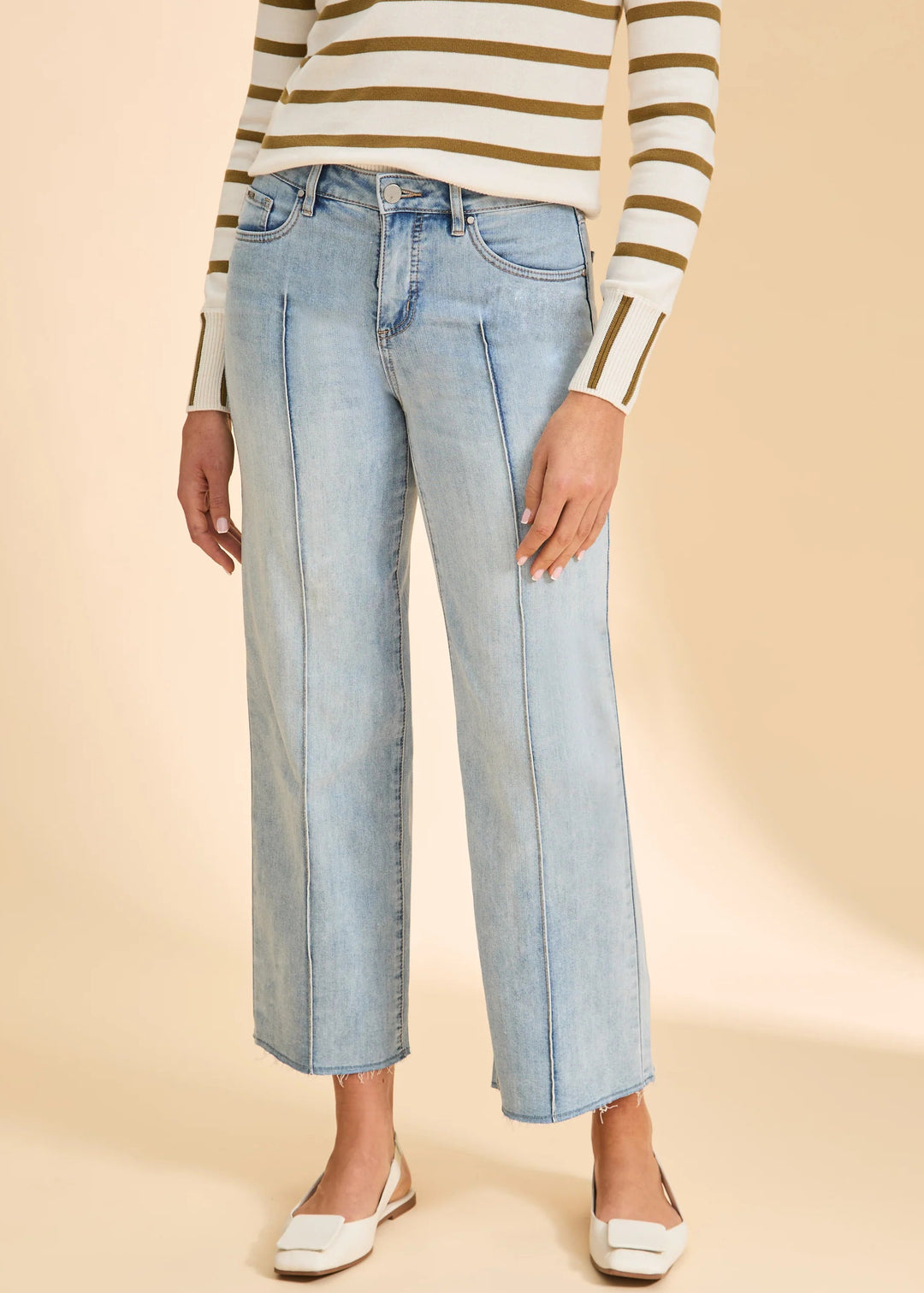 Person wearing light blue jeans and a striped sweater on a beige background