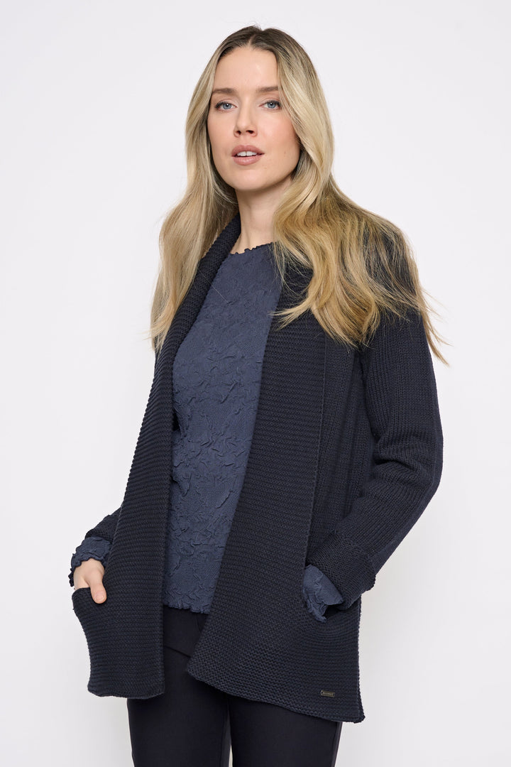 A woman modeling a dark navy textured open-front cardigan over a dark blue knit top and black pants, photographed against a clean white studio background.