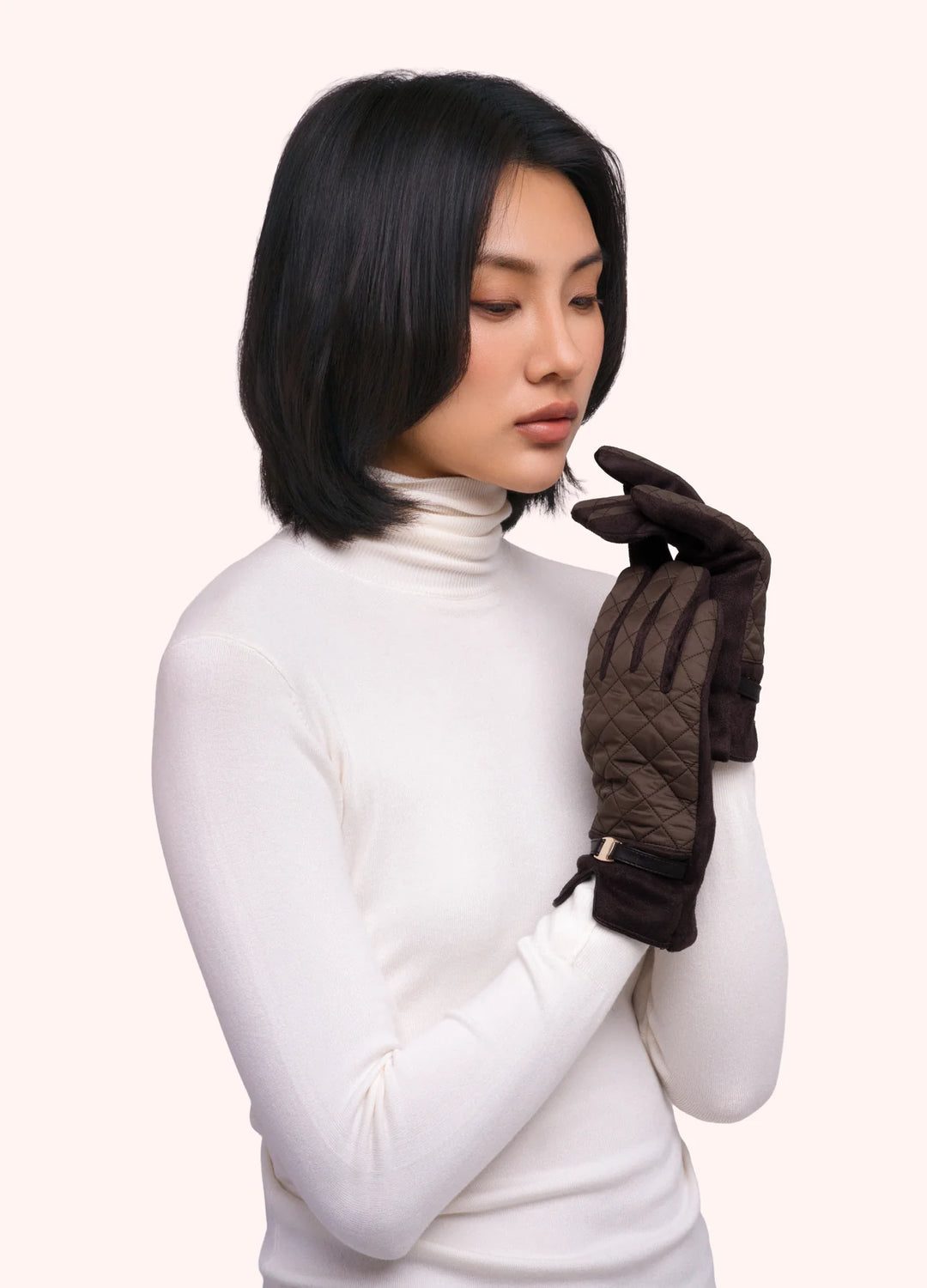 Woman wearing a white turtleneck and dark gloves on a plain background