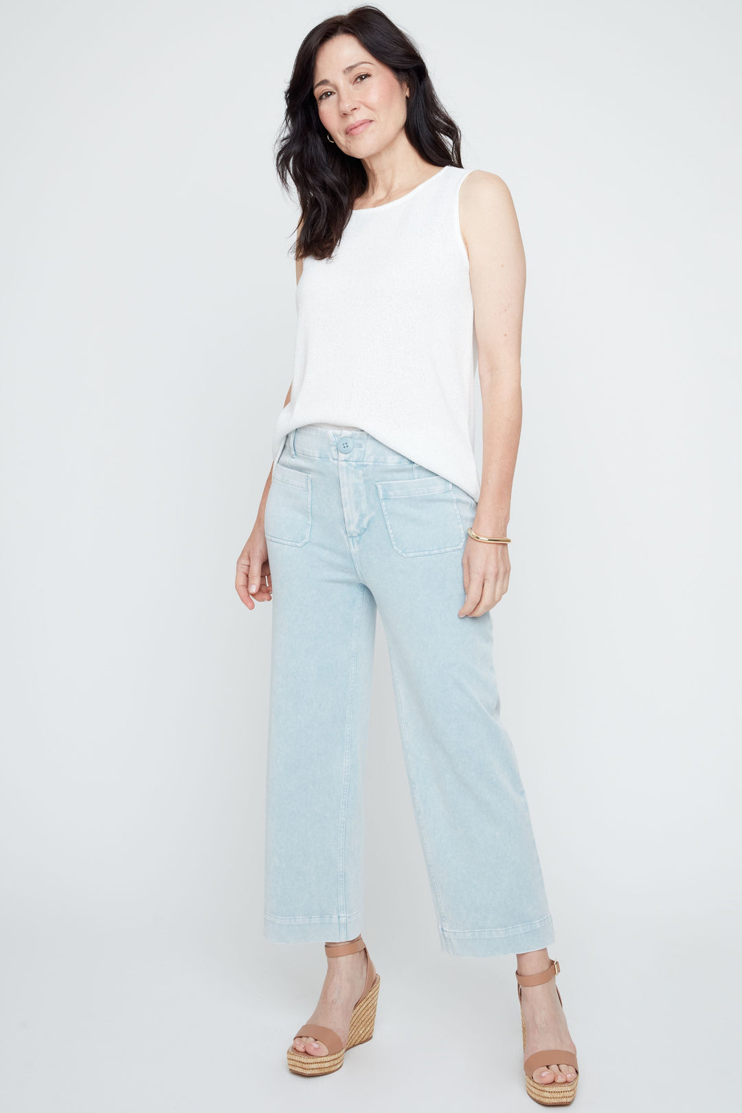 Woman wearing a white sleeveless top and light blue jeans on a white background