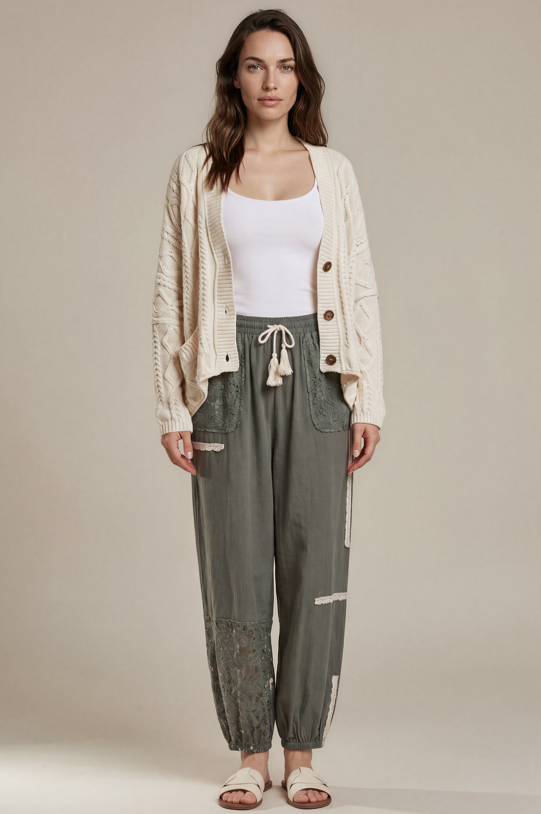 Woman wearing a white cardigan, white top, and green pants on a beige background