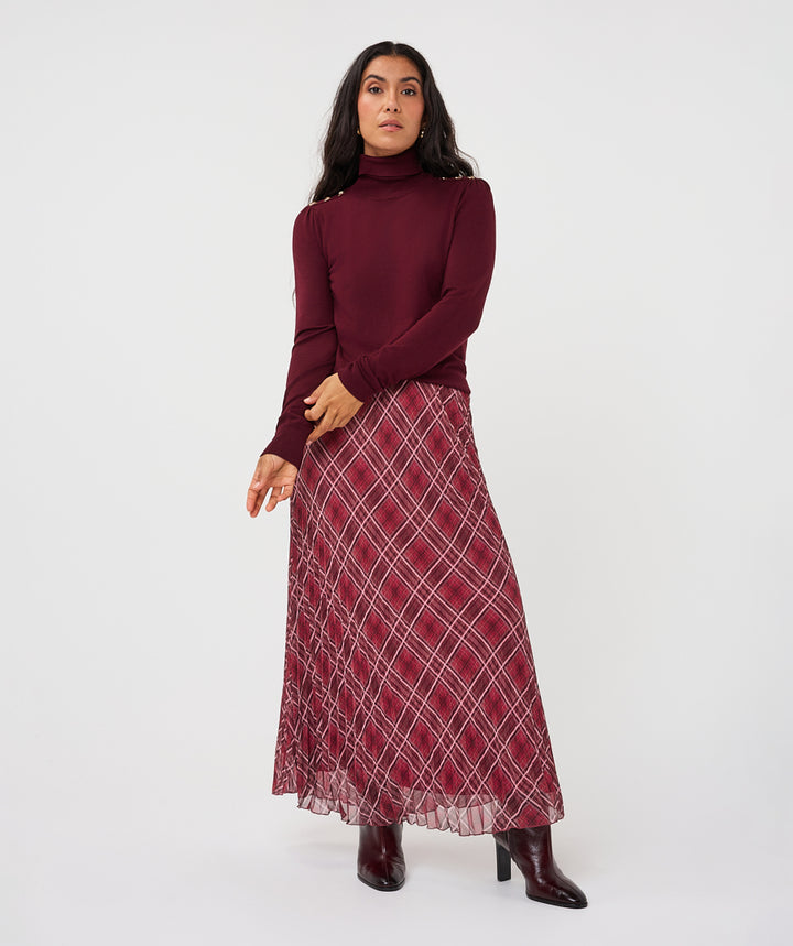 A woman modeling a long-sleeve burgundy turtleneck sweater and a matching burgundy maxi skirt with a white plaid pattern, paired with dark burgundy ankle boots, against a plain white studio background.
