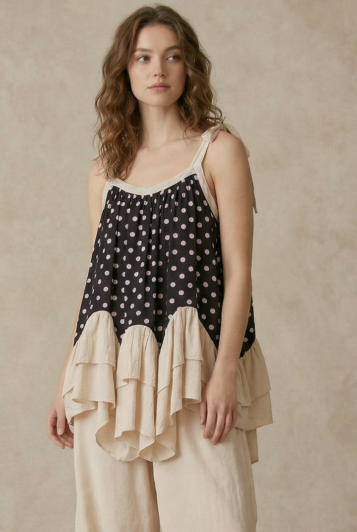 Woman wearing a polka dot top with ruffled layers and beige pants against a beige background