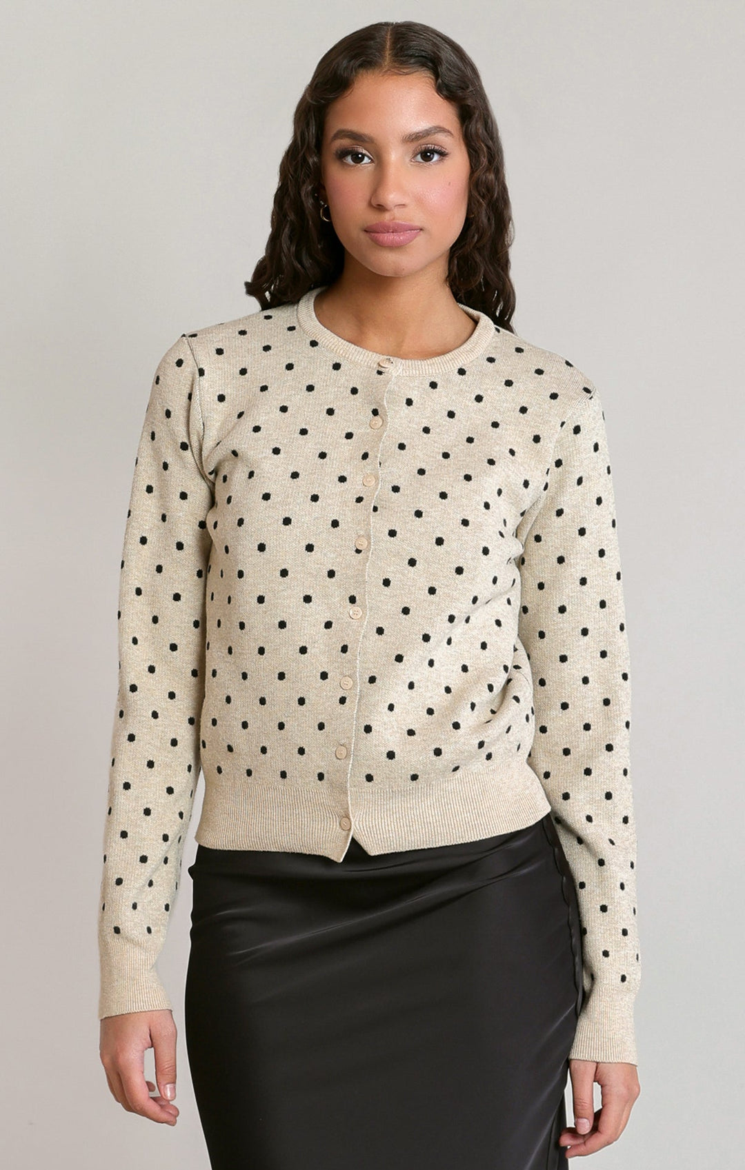Woman wearing a beige polka dot blouse with a plain background