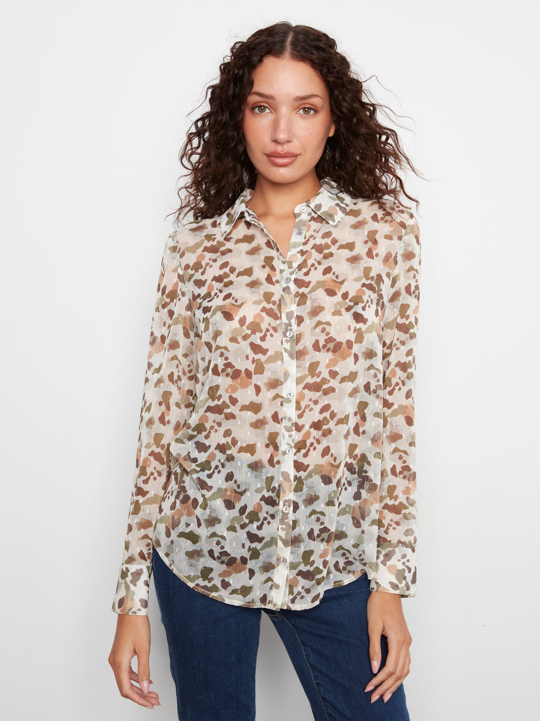 A woman modeling a long-sleeve button-up blouse with a brown and beige leopard print on a cream background, paired with dark blue jeans, against a plain white studio background.