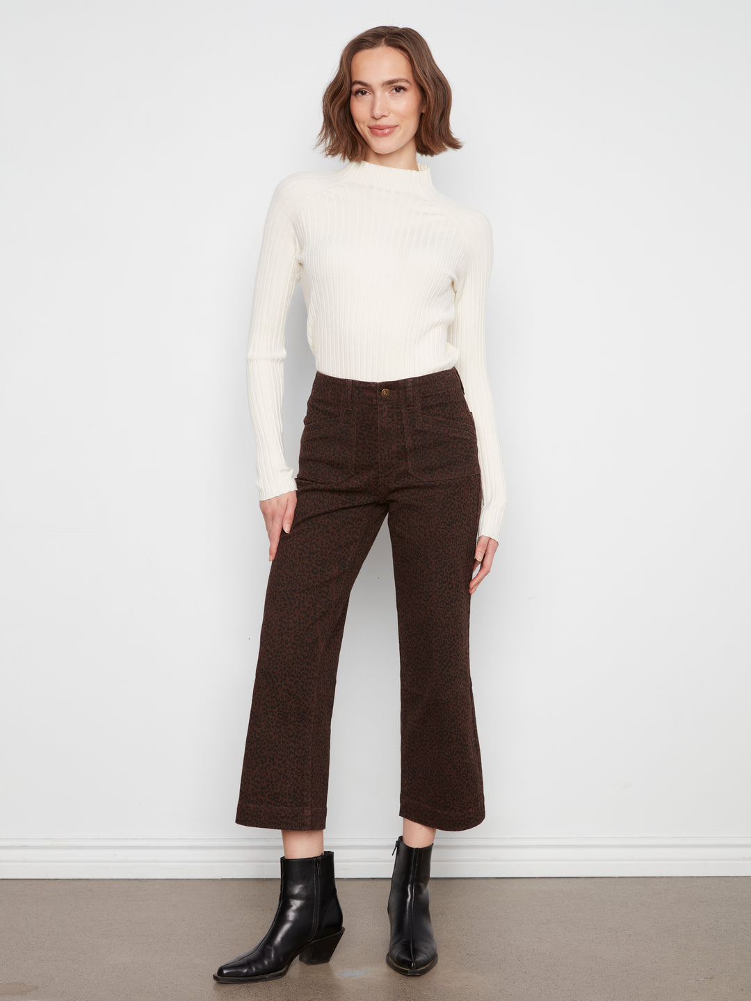 Woman wearing a white sweater and brown pants against a white background