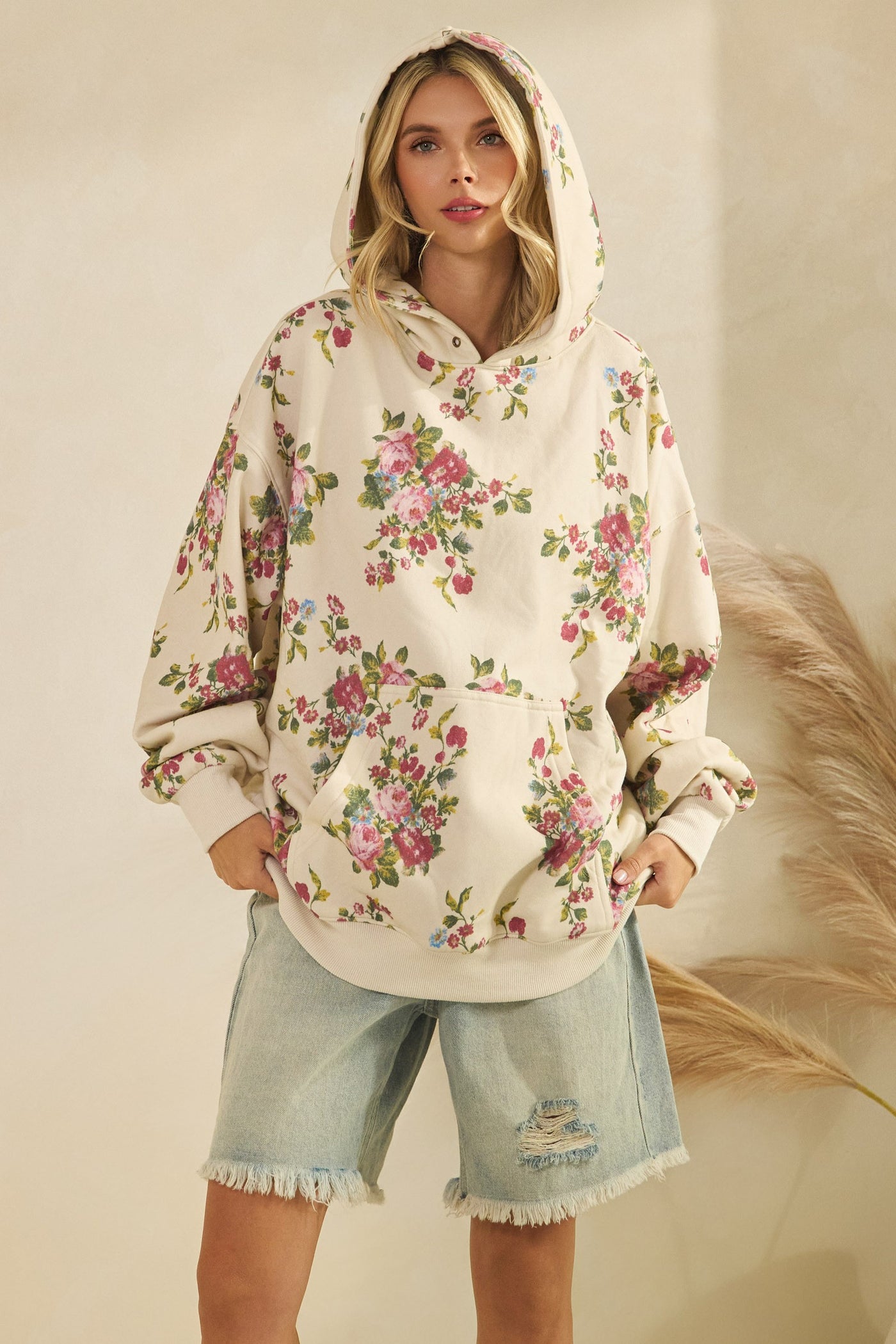 Woman wearing a floral hoodie and denim shorts on a neutral background