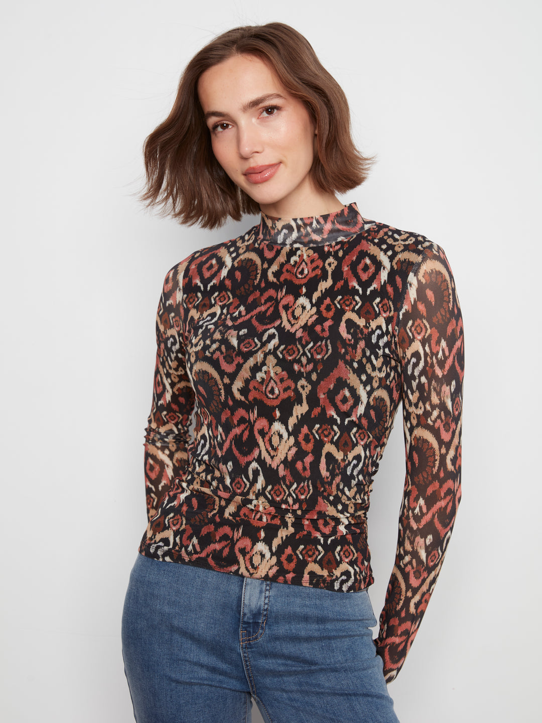 Woman wearing a patterned long-sleeve top and jeans on a white background