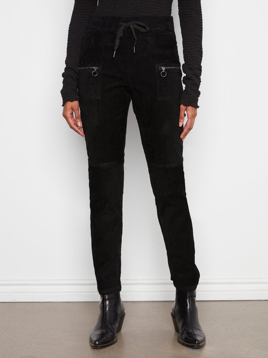 Person wearing black pants and black shoes against a white wall