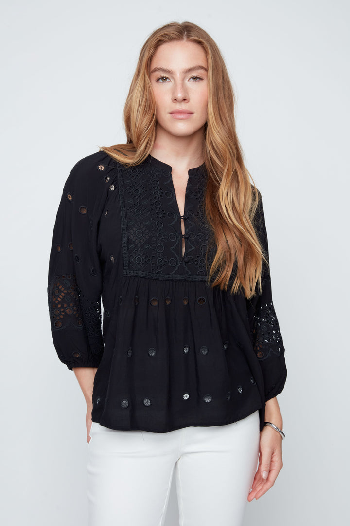 Woman wearing a black lace top with white pants on a plain background