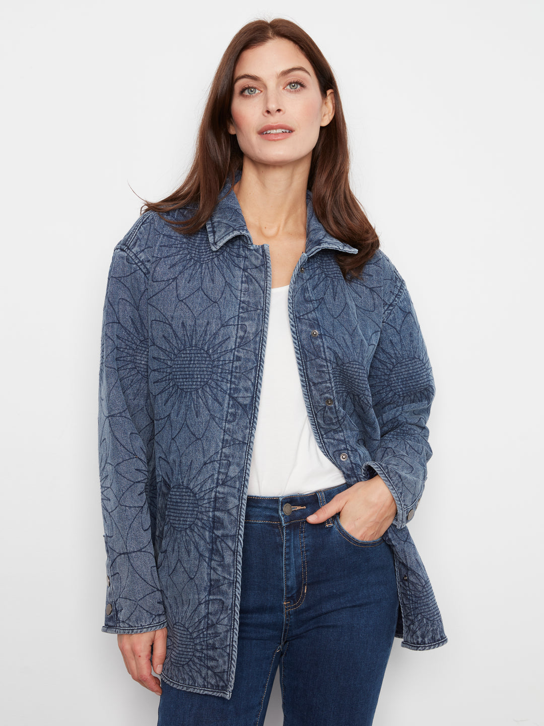 A woman modeling a blue textured denim jacket with a white top and dark blue jeans against a plain white background.