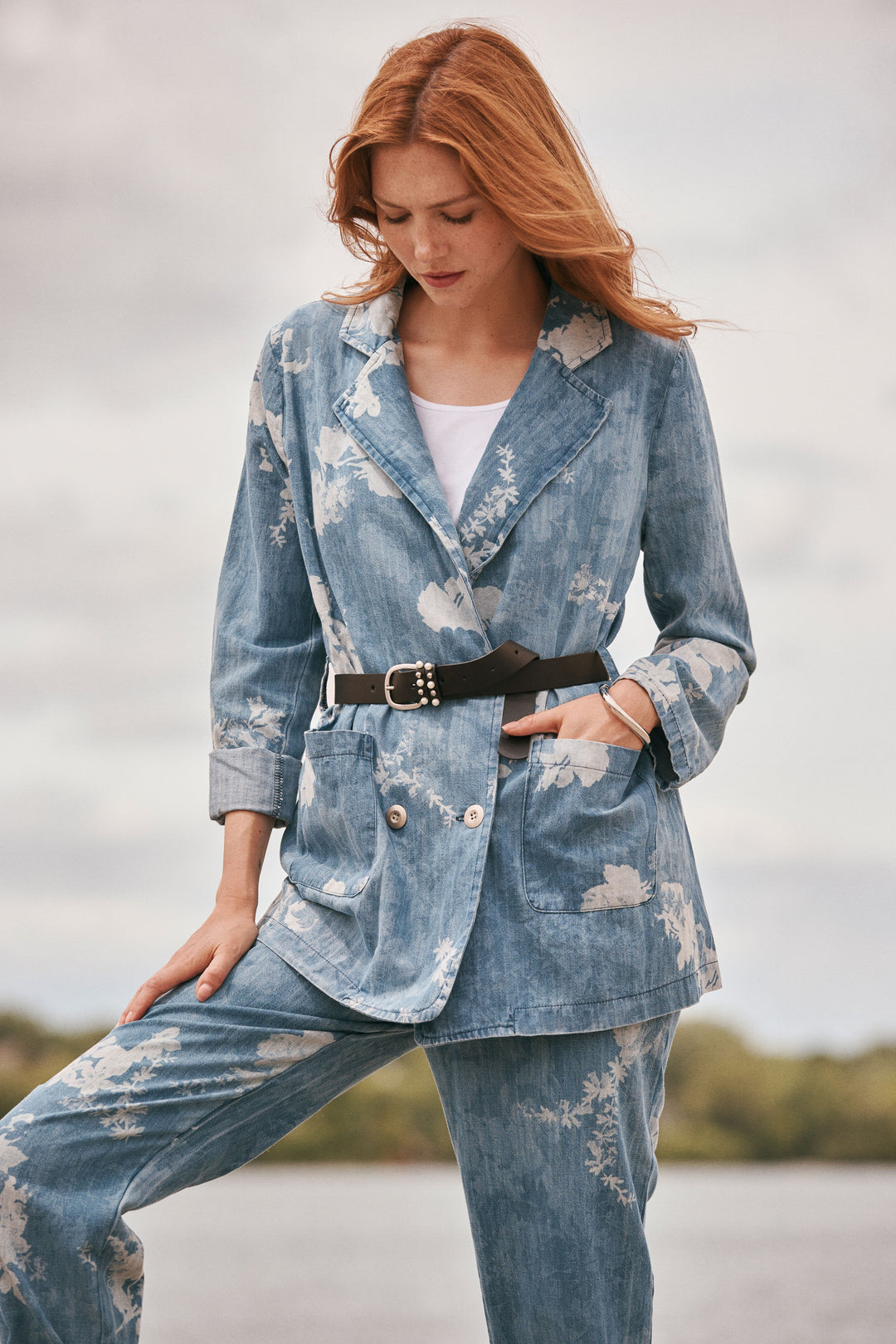 Woman wearing a blue floral blazer and jeans with a blurred natural background