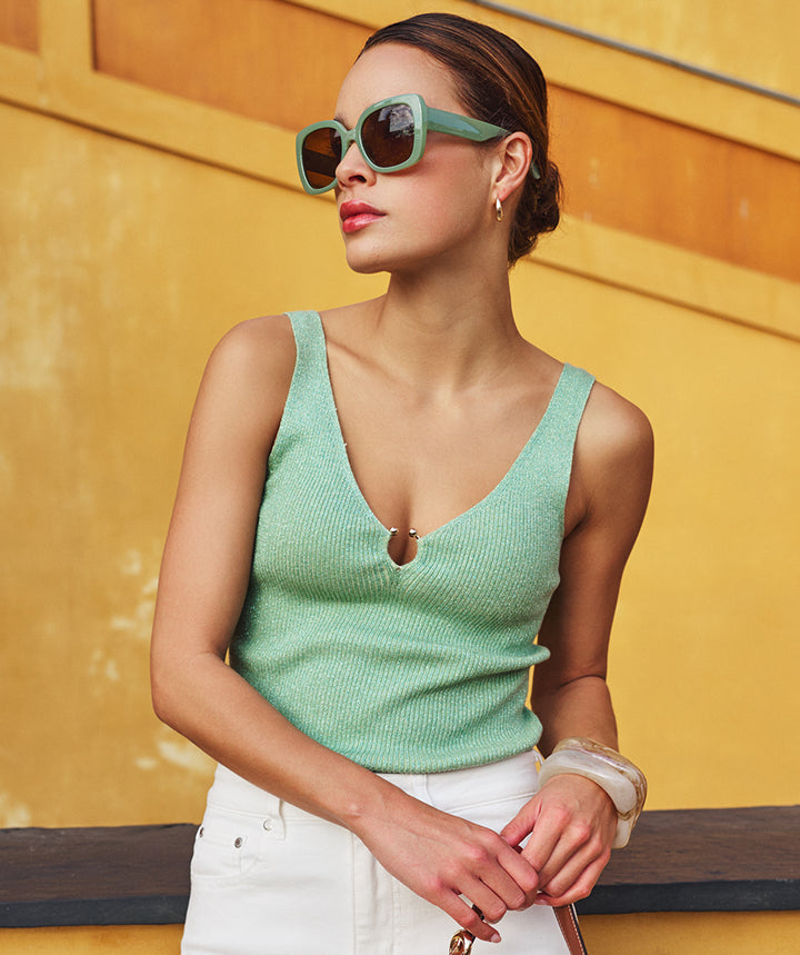 Woman wearing a green tank top and sunglasses against a yellow wall