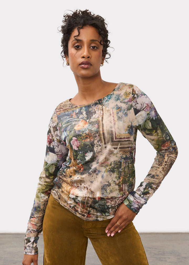 A woman modeling a long-sleeve top with a vintage, multicolored scenic print, paired with wide-leg mustard brown trousers, against a neutral studio background.