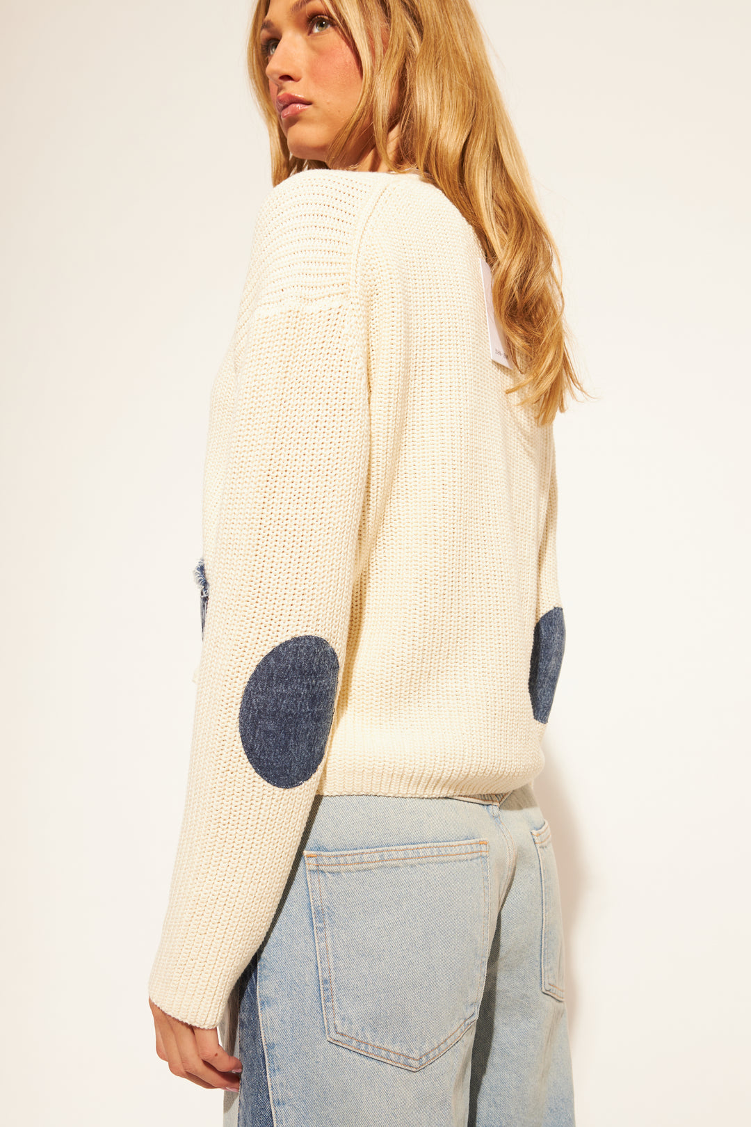 Woman wearing a cream sweater with blue polka dot sleeves against a plain background