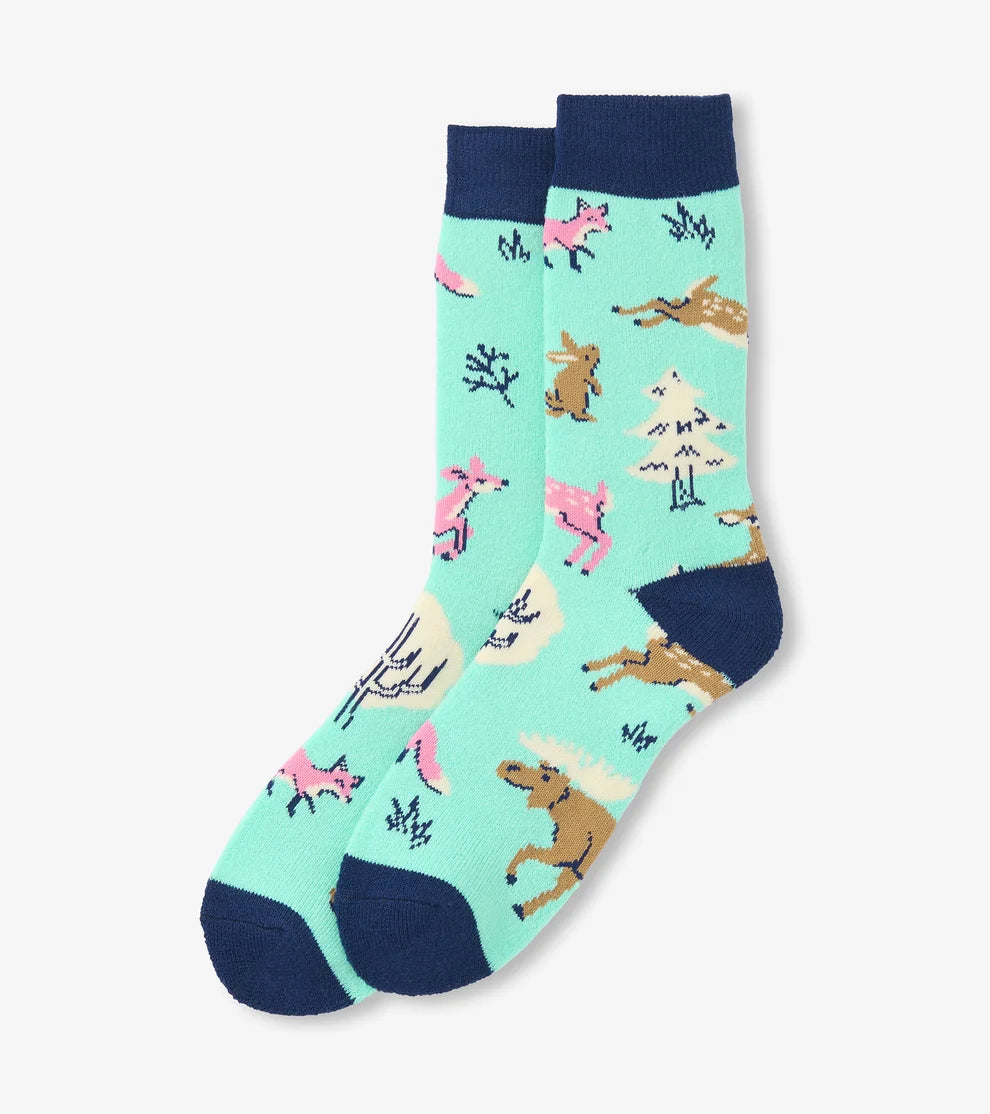 A pair of crew socks with a light mint green background featuring a whimsical pattern of brown deer, pink foxes, and small trees, finished with dark navy blue heels, toes, and cuffs.