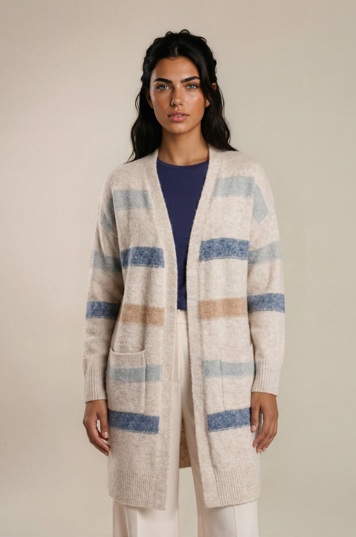 A woman modeling a long open-front knit cardigan with horizontal stripes in blue, beige, and light gray on an off-white base, worn over a navy top and cream pants against a plain beige studio background.