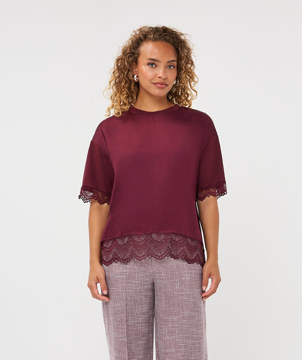 A woman modeling a two-piece loungewear set consisting of a short-sleeve maroon top with lace trim and matching wide-leg mauve pants, photographed against a plain white studio background.