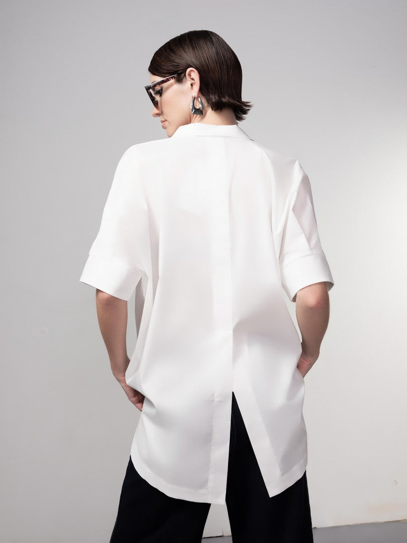 Person wearing a white oversized shirt with black pants on a plain background