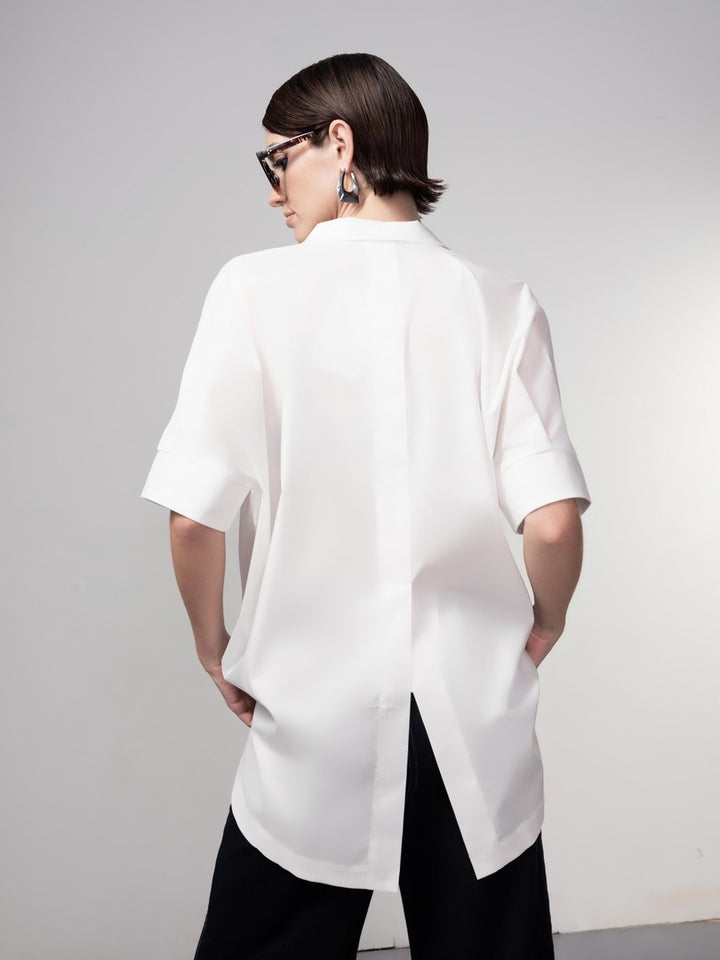 Person wearing a white oversized shirt with black pants on a plain background