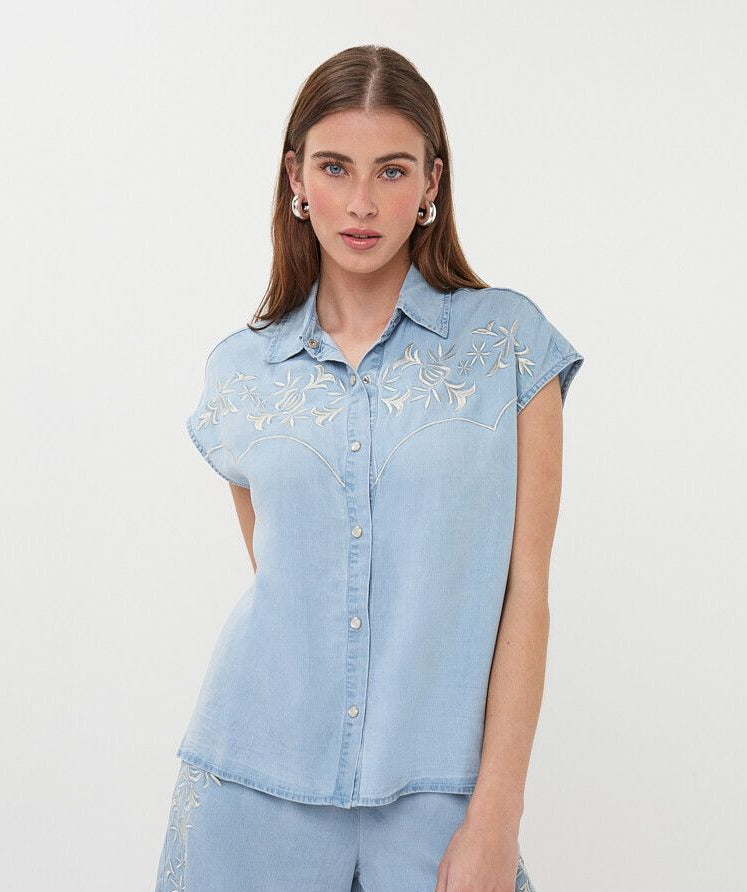 Woman wearing a light blue denim outfit with floral embroidery on a white background