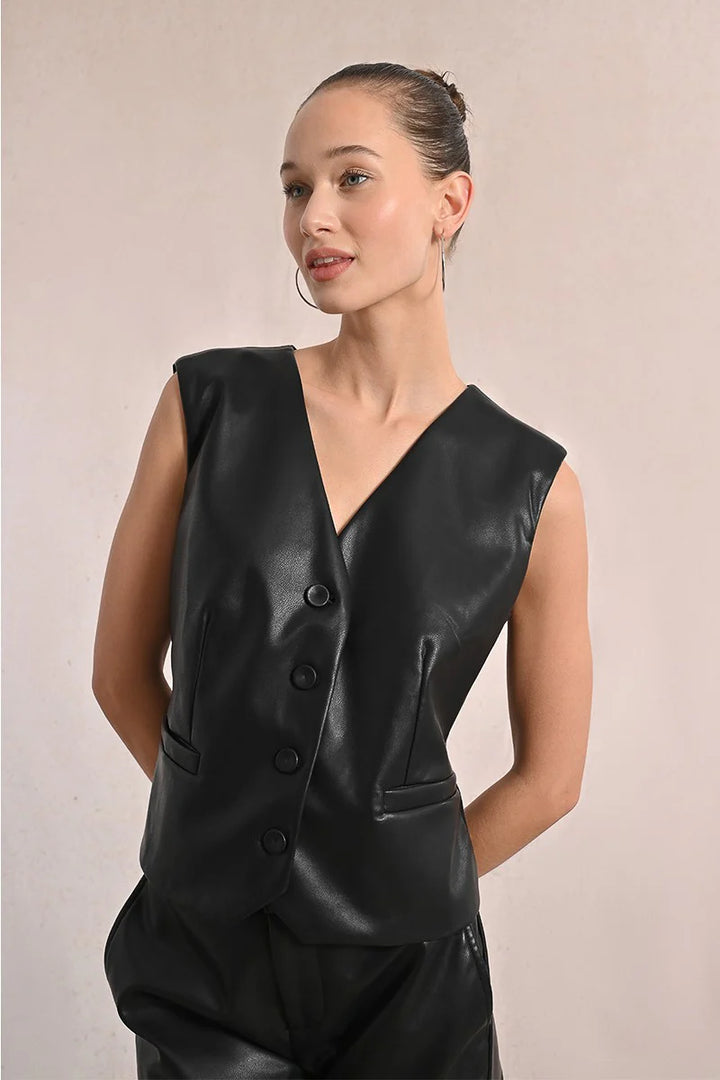 Woman wearing a black leather vest against a plain background