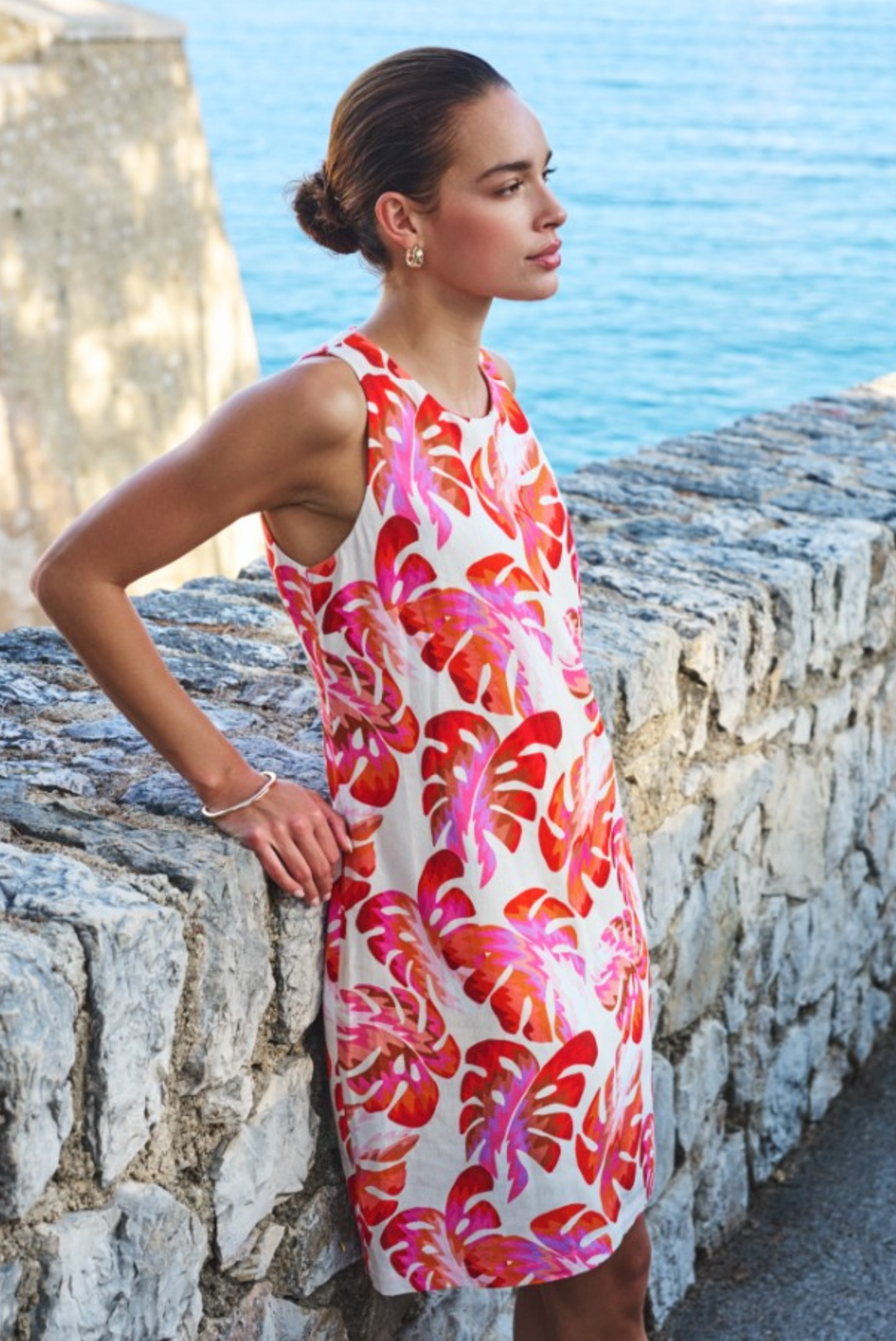Woman in a colorful dress standing by a stone wall with ocean view
