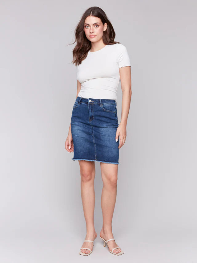 Woman wearing a white t-shirt and blue denim skirt on a gray background