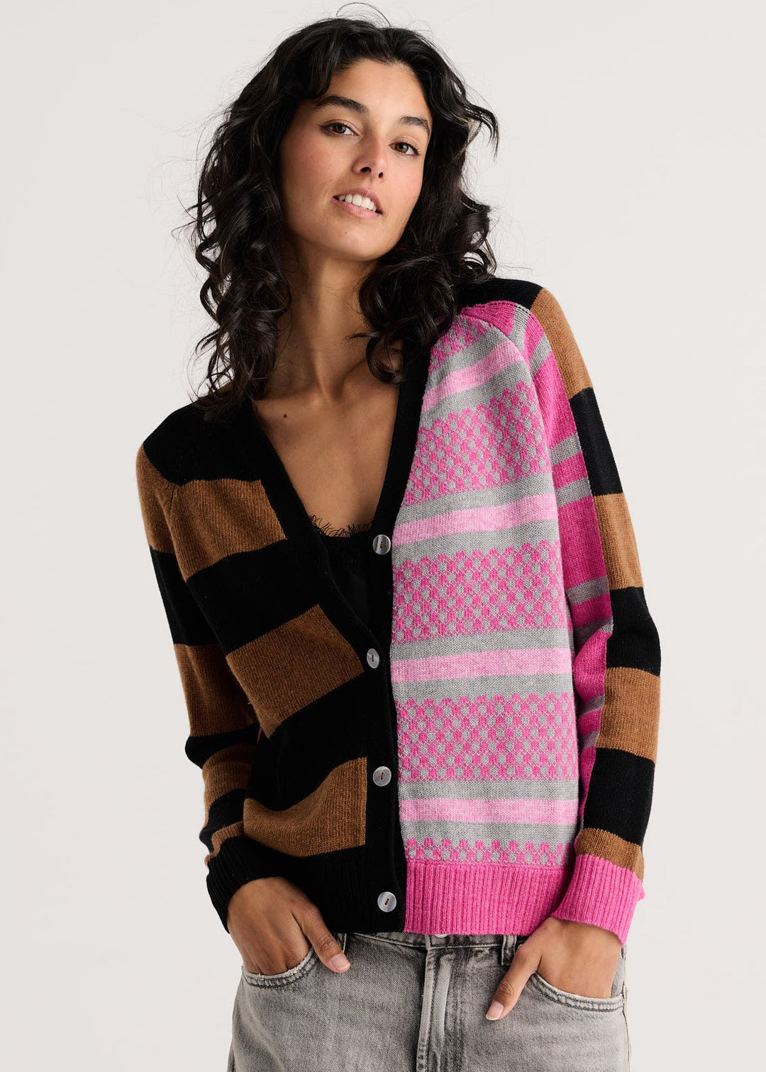 A woman modeling a color-block knit cardigan with pink, brown, black, and gray stripes, paired with light gray jeans, against a plain light gray background.