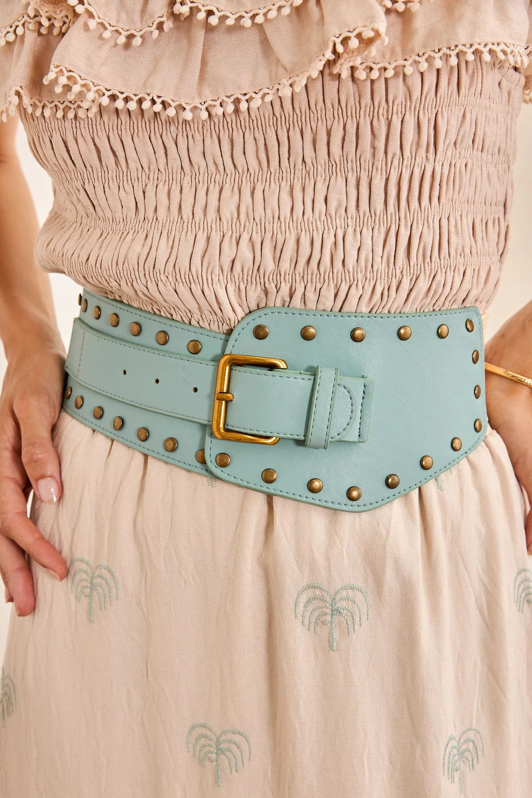 Light blue belt with gold buckle worn by a person in a beige dress.