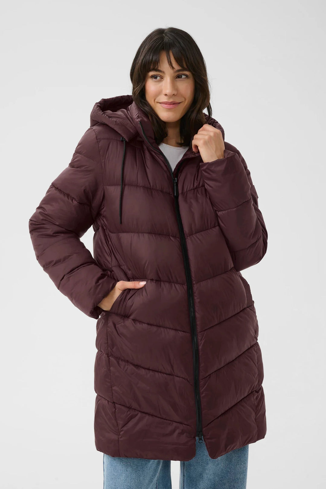 Woman wearing a long burgundy puffer coat on a white background