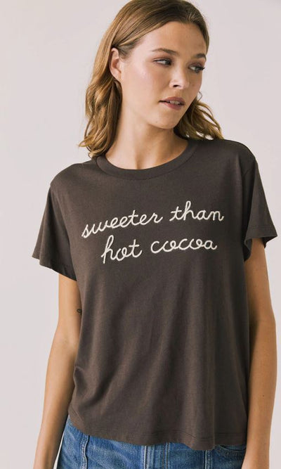 Woman wearing a brown t-shirt with 'sweeter than hot cocoa' text on a plain background
