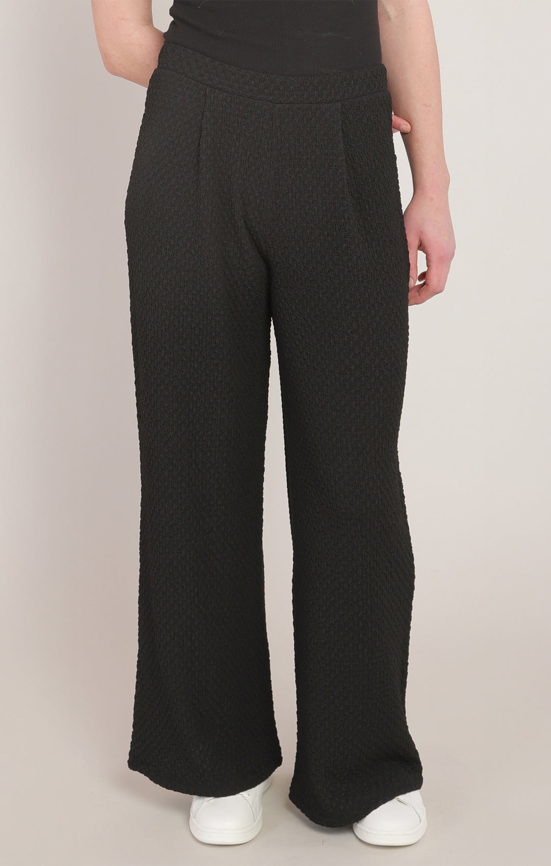 Person wearing black textured wide-leg pants on a plain background
