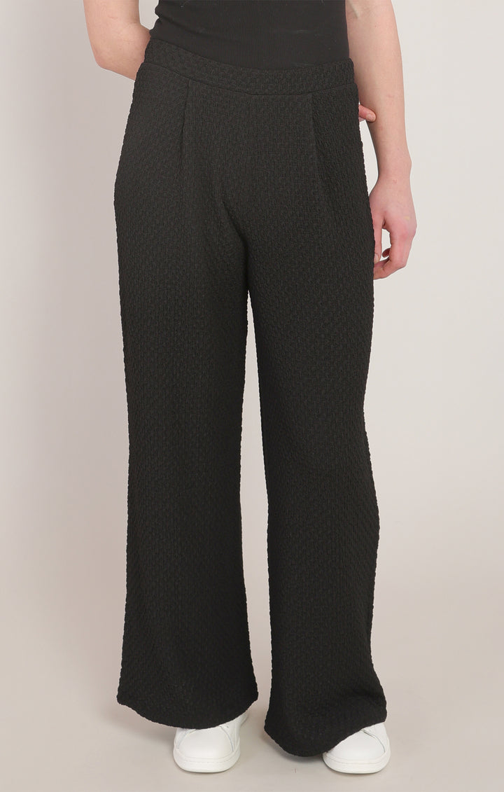 Person wearing black textured wide-leg pants on a plain background