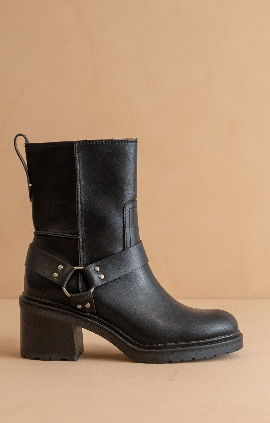 Black leather boot with buckle detail on a beige background