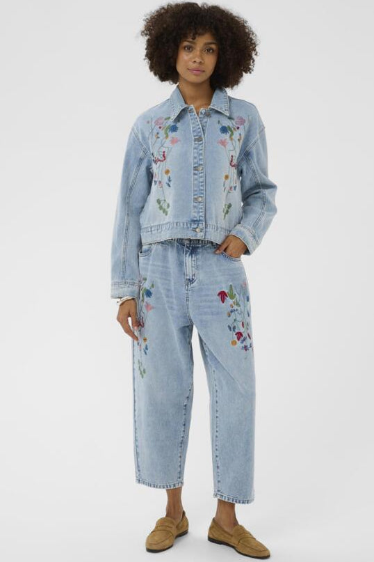 Woman wearing an embroidered denim jacket and jeans on a white background
