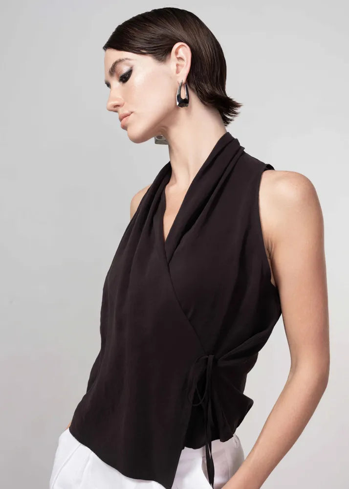Woman wearing a black sleeveless top with a draped design on a gray background