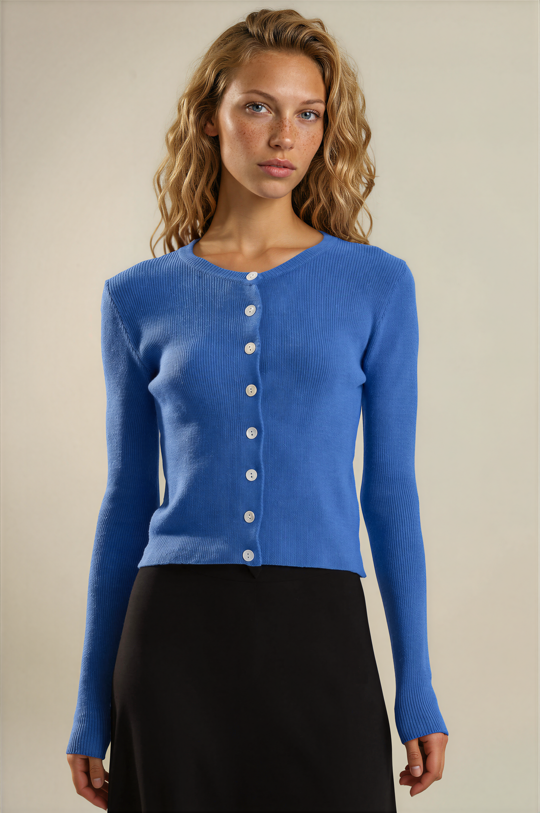 A woman modeling a bright blue long-sleeve knit cardigan with a button-front closure, paired with a black skirt, against a plain beige studio background.