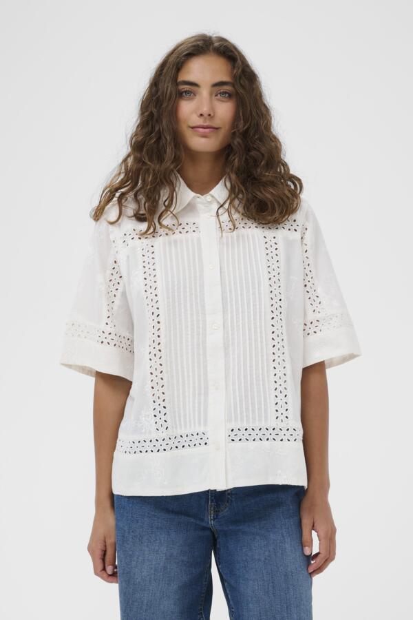 Woman wearing a white blouse with lace details on a plain background