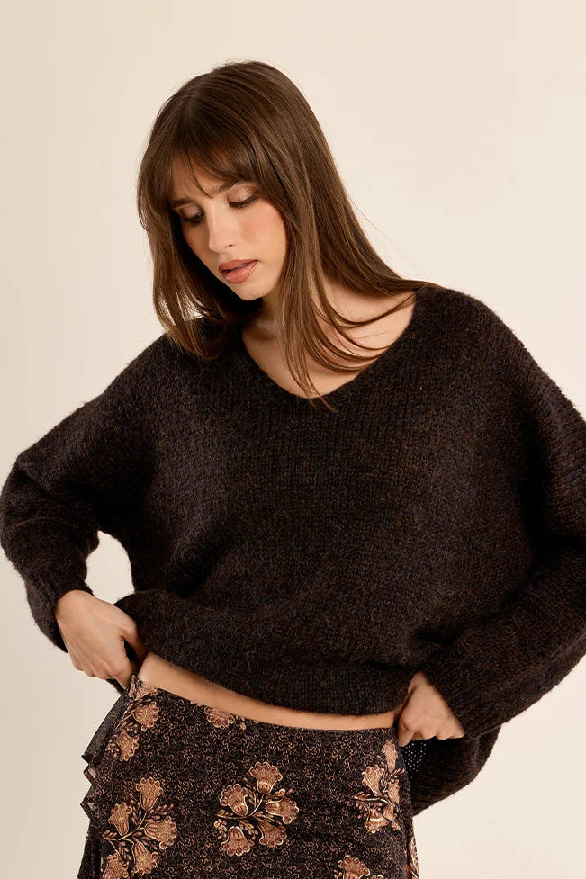 A woman wearing a dark brown fuzzy knit sweater and a dark brown floral skirt, posing against a solid light beige background.