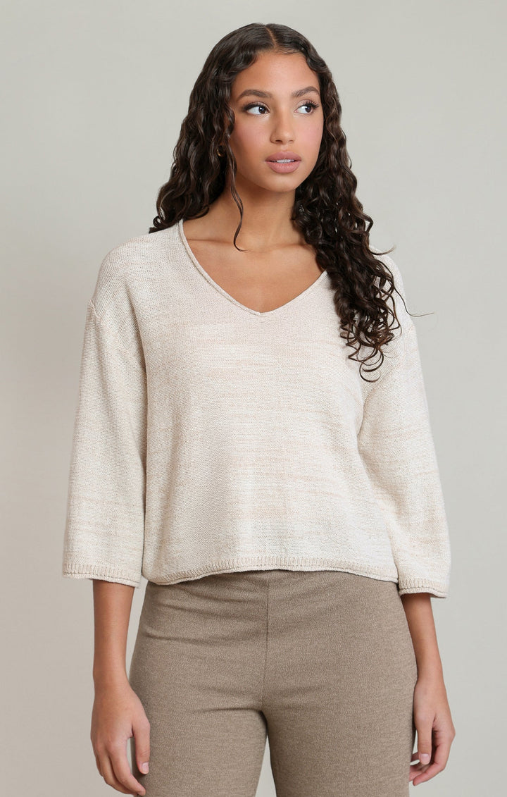 Woman wearing a beige sweater and brown pants against a neutral background