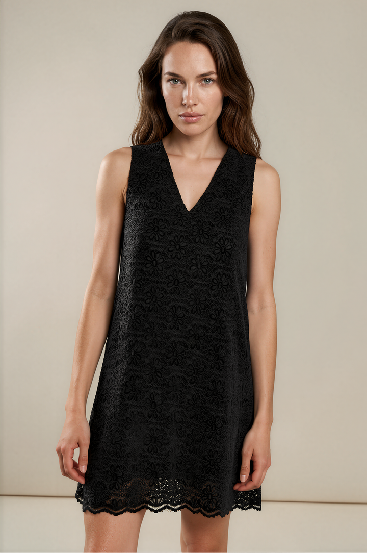 A woman modeling a sleeveless black lace mini dress with a V-neckline against a plain beige studio background.