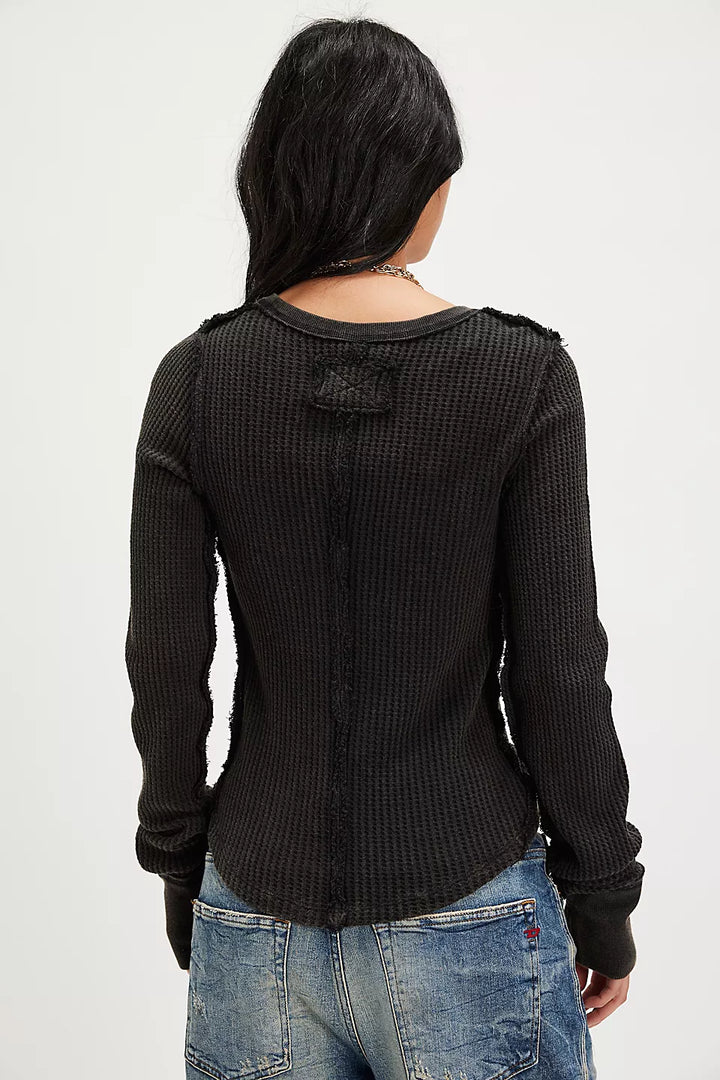 A woman viewed from the back wearing a black textured long-sleeve top and blue jeans against a plain light background.