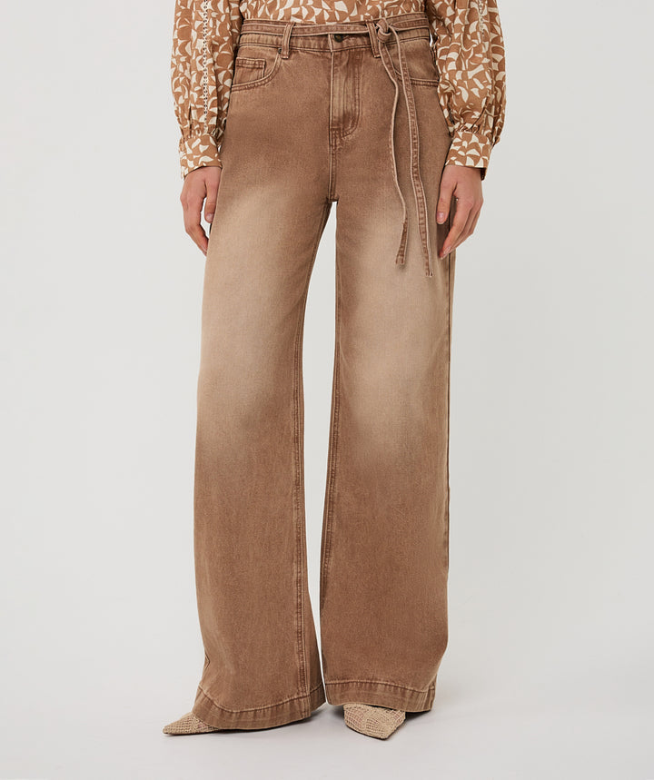 Person wearing brown wide-leg jeans and a patterned shirt on a light gray background