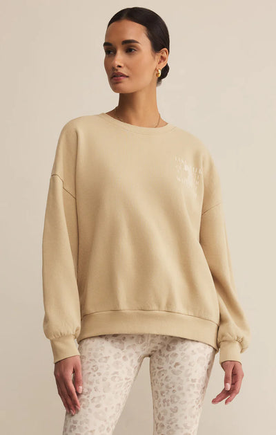 Woman wearing a beige sweatshirt and patterned pants on a plain background