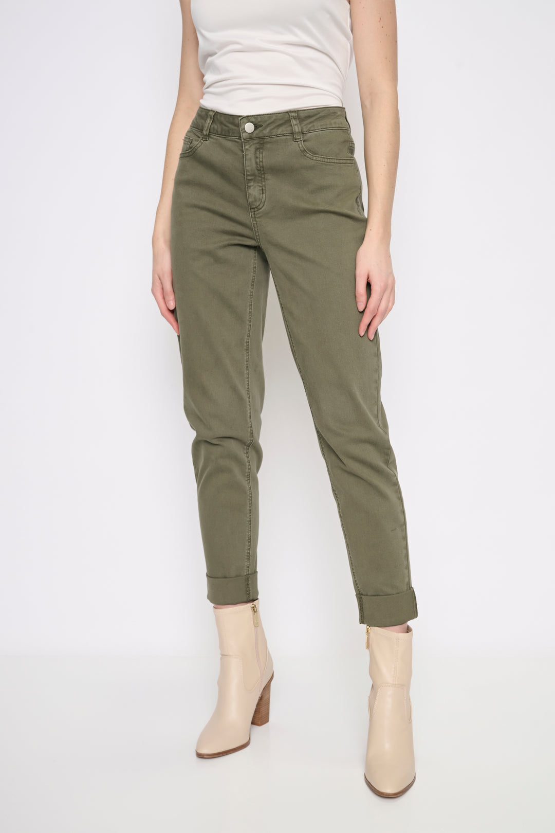 A model wearing olive green cropped jeans with rolled cuffs, paired with a white tank top and beige ankle boots, shown against a plain white studio background.